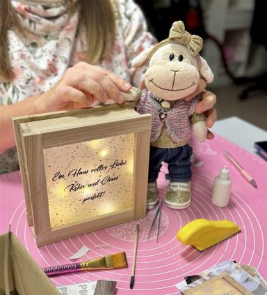 Eine Person stellt eine beleuchtete Box neben eine Stofffigur eines Schafes.